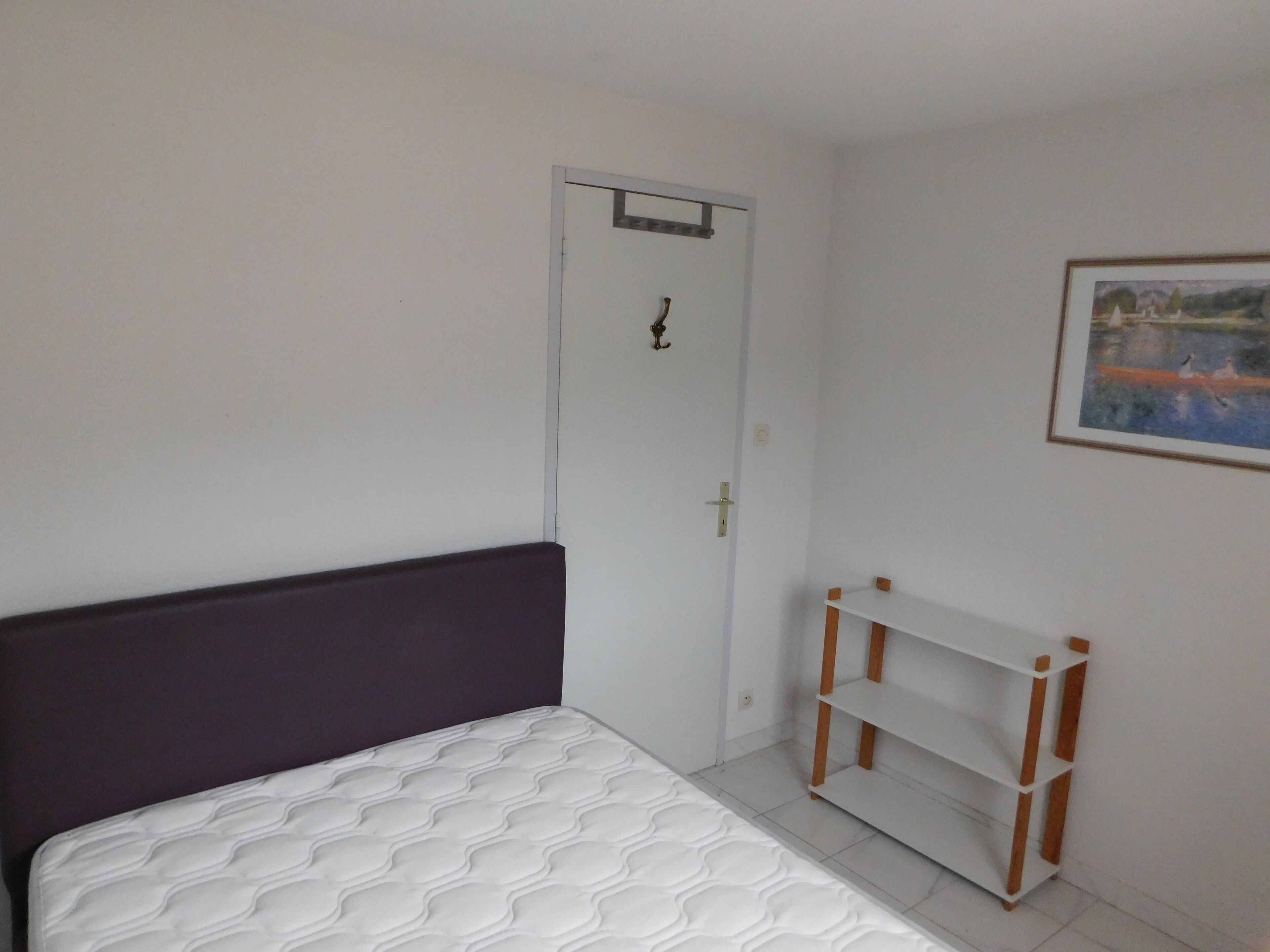 A bedroom with a bed, a door, a shelf, and a painting on the wall.