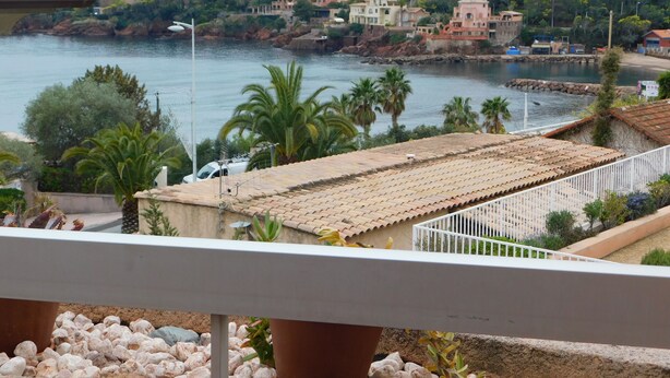 A coastal town with terracotta-roofed buildings, a rocky shoreline, and palm trees. - F9 Large bright apartment, 3 rooms, beach at 50m, swimming pool and sea view  (Théoule Sur Mer)