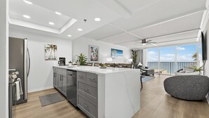 Een moderne keuken met een centraal eiland, een eetgedeelte met uitzicht en een woonruimte met een balkon over de zee.