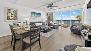 Een ruime woonkamer met een eettafel, banken en een balkon met uitzicht op het strand.