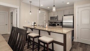 Una cocina con encimera de granito, electrodomésticos de acero inoxidable e iluminación colgante.