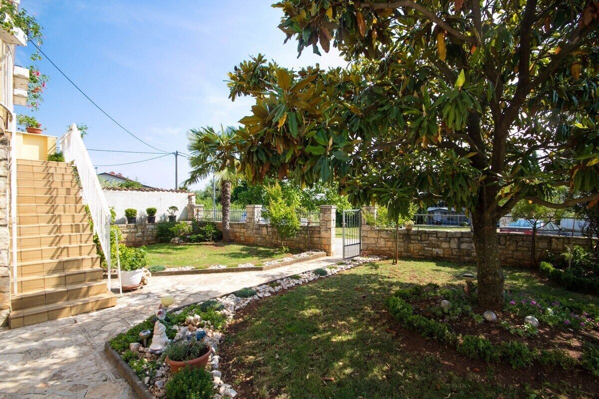 A garden with a stone wall, a tree, and a paved pathway leading to a gate.