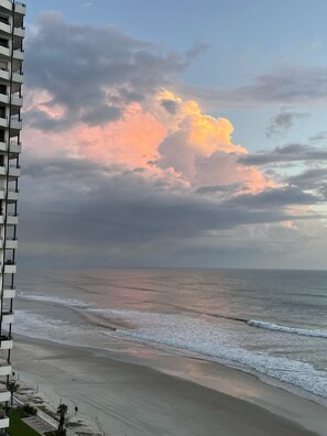 Un immeuble de grande hauteur surplombant une plage, avec des vagues et un ciel nuageux.
