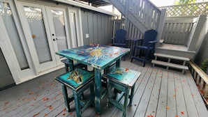 Eine Holzterrasse mit Tisch und Stühlen, umgeben von einem grauen Zaun und einer Treppe.