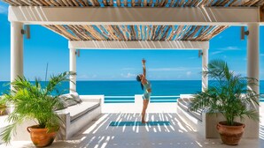 Un espacio al aire libre cubierto con vista al mar, una colchoneta de yoga y plantas en macetas.
