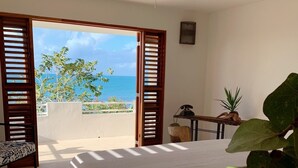 Un dormitorio con cama, ventilador de techo y vista al océano a través de contraventanas abiertas.