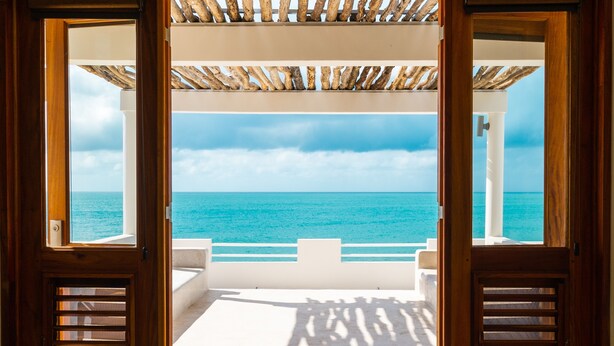 Una puerta de madera abierta que da a un balcón con vistas al mar y un cielo nublado.