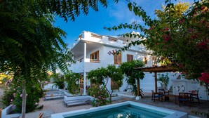Una villa blanca con piscina, rodeada de vegetación y mobiliario de exterior.