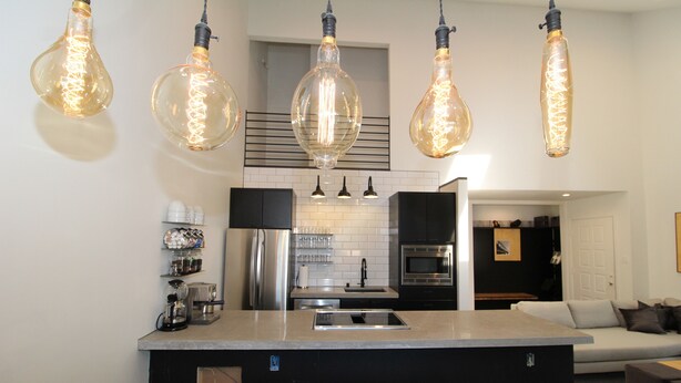 Une cuisine moderne dotée d’un îlot central, d’appareils électroménagers en acier inoxydable et de luminaires suspendus.