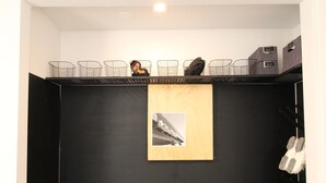 Une petite pièce sombre, avec un banc en bois, un tableau encadré au mur et une étagère contenant des paniers et des boîtes en fil de fer.