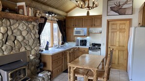 A rustic kitchen with a stone wall, wooden cabinets, a central island, and a fireplace. - Aspen Cabin at Rye Creek Lodge (Darby)