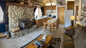 A cozy cabin interior with a stone fireplace, wooden furniture, and a kitchen area. - Aspen Cabin at Rye Creek Lodge (Darby)