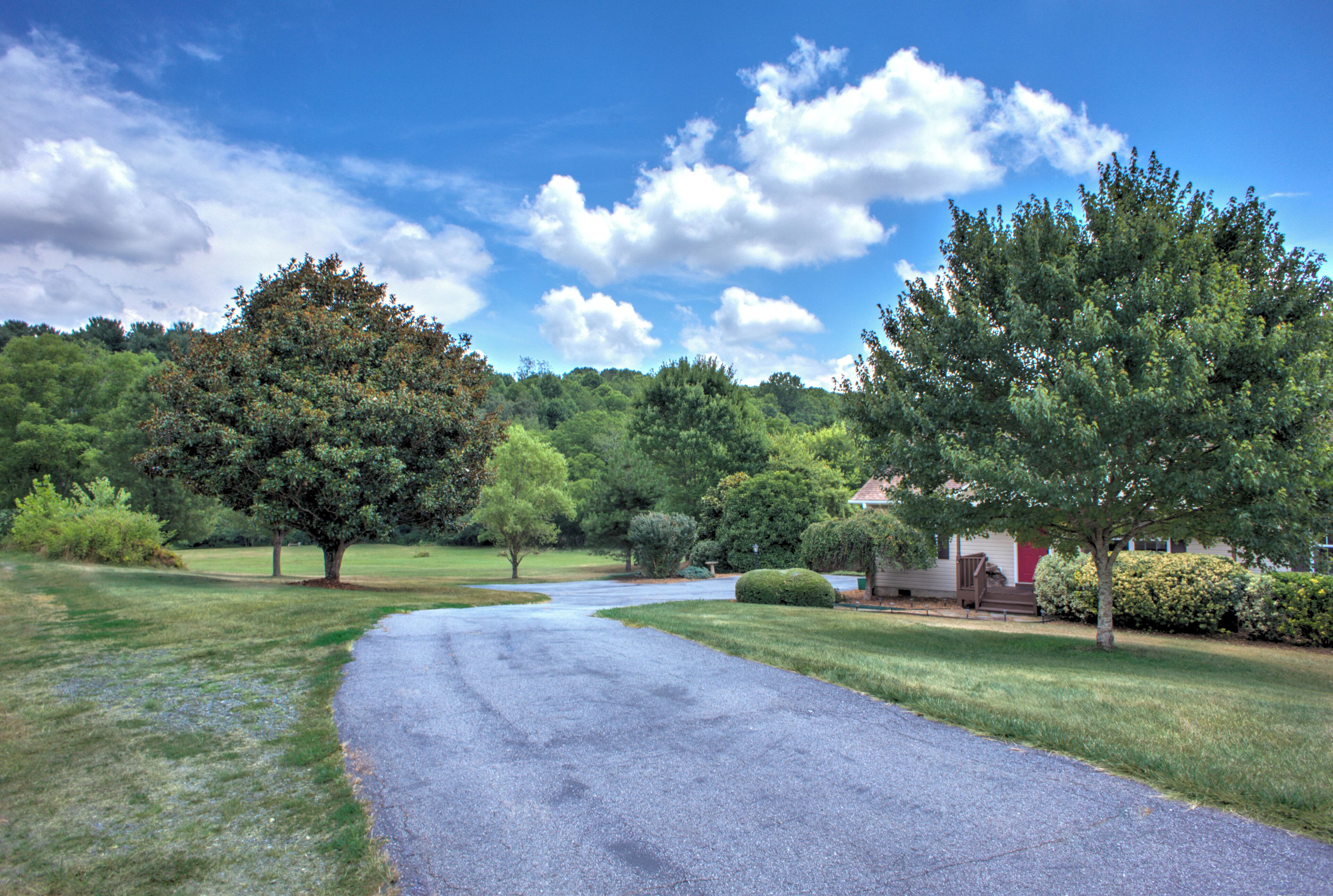 A residential driveway with a house, trees, and a clear sky.