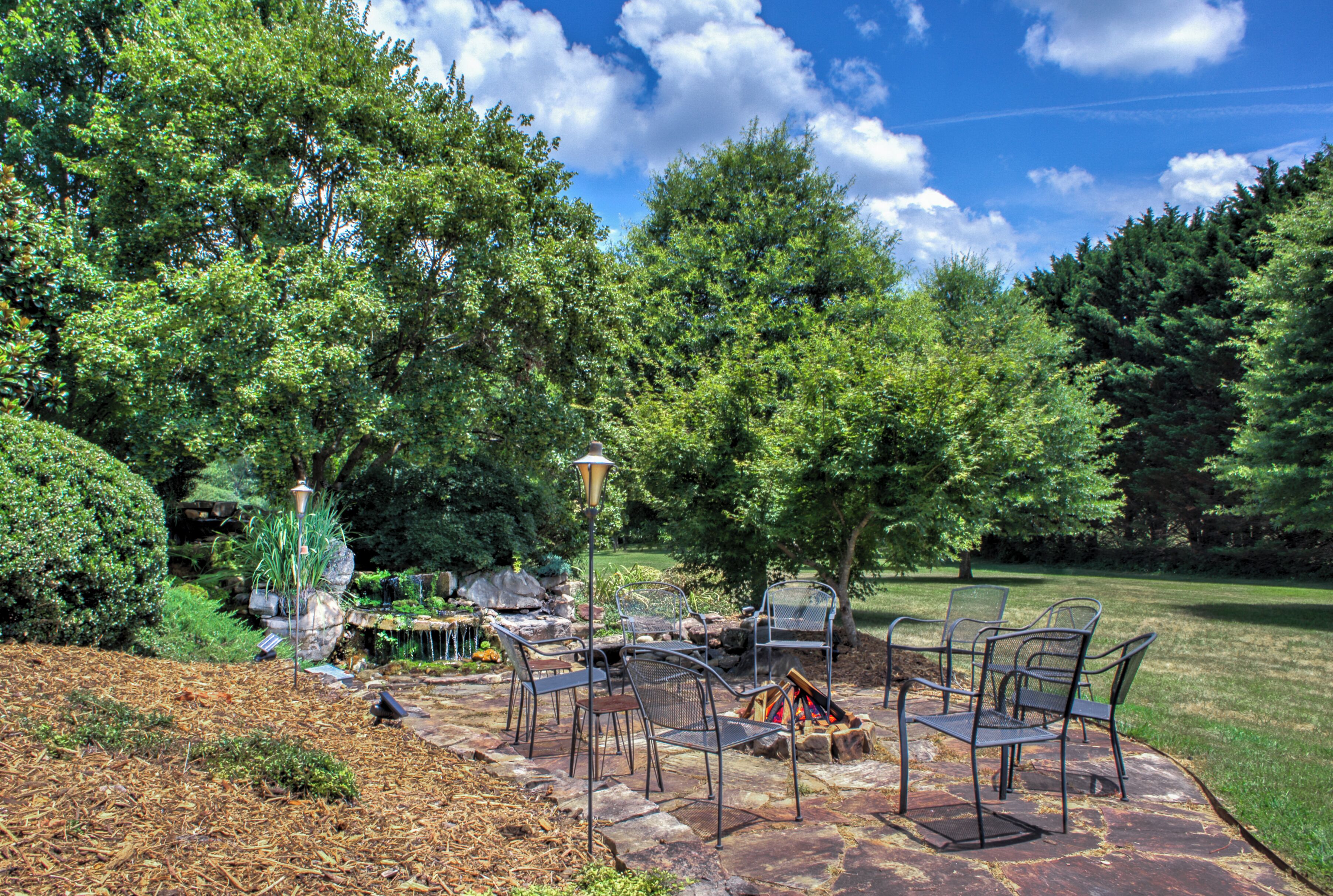 An outdoor patio with stone flooring, metal chairs, a fire pit, and a small table with a lamp.