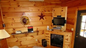 A cozy cabin interior with a wooden wall, a fireplace, a television, and a sofa. -  Romantic Log Cabin On Creek And 100 Acres, Hot Tub, Wifi, Gas Grill, Hiking (Hot Springs)