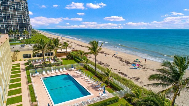 A hotel with a pool, beach view, and palm trees.