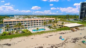 A hotel with multiple floors, a swimming pool, and a beach area with umbrellas.