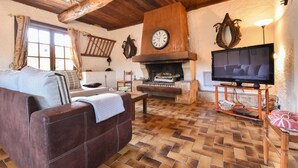 Ein gemütliches Wohnzimmer mit Kamin, Holzbalken, einem Fernseher und einer Couch.