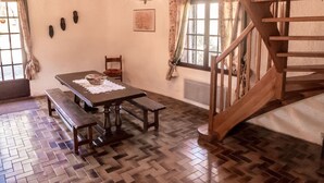 Ein Essbereich mit Holztisch, Bänken und einer Chandelüster. Eine Treppe mit Holzwertkappen und ein Fenster mit Vorhängen sind ebenfalls vorhanden.