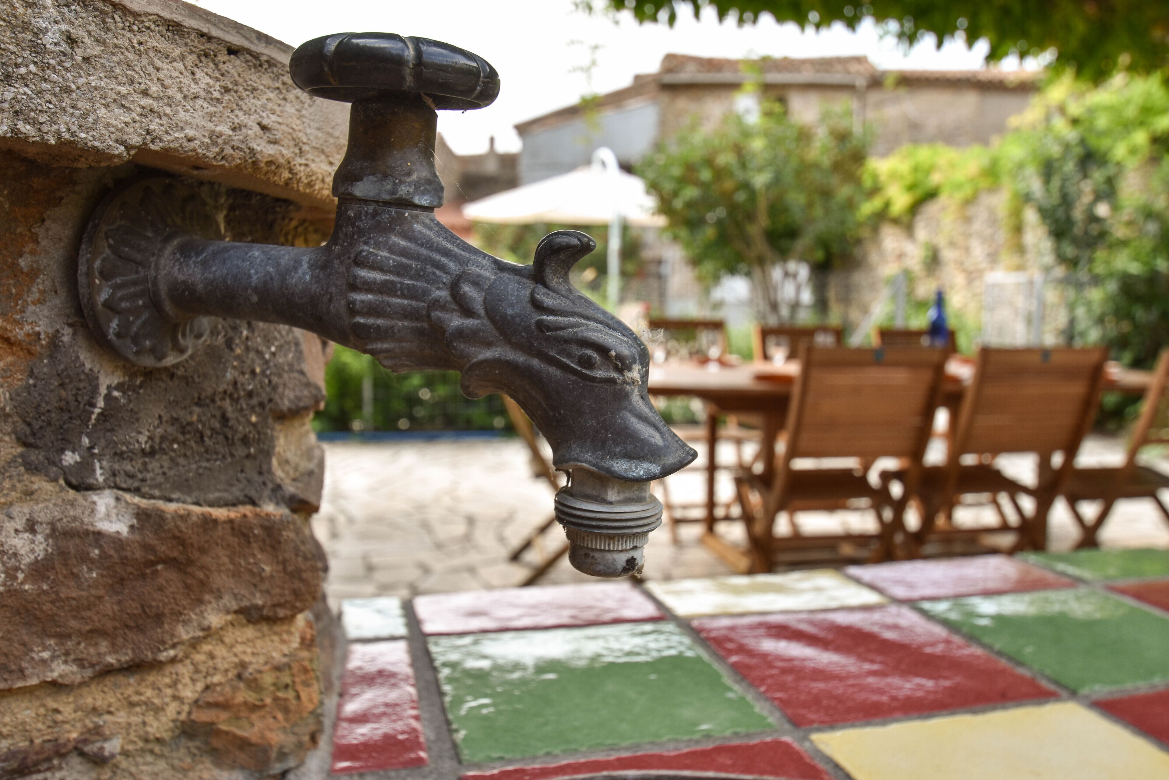 Un grifo instalado en una pared de piedra, con un patio empedrado al fondo.