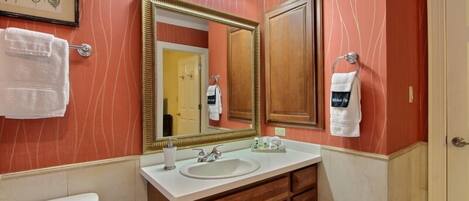 A bathroom with a large mirror, a sink, and wooden cabinets. There are towels hanging on the wall and a toilet visible.