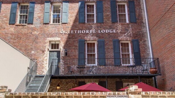 A brick building with the name "OGLETHORPE LODGE" on the facade. There is a staircase leading to the entrance, and a sign indicating private parking. - 1bd, 1.5ba Historic District and River Front-Walk to Everything! (Savannah)