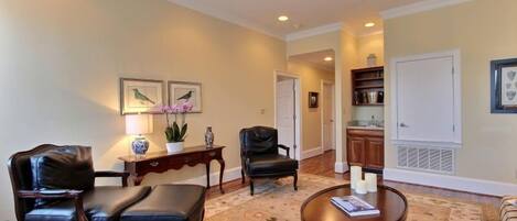 A living room with a round wooden coffee table, two black leather chairs, a floral patterned rug, and a bookshelf.