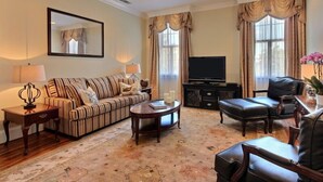 A living room with a striped sofa, a coffee table, a television, and leather chairs. - 1bd, 1.5ba Historic District and River Front-Walk to Everything! (Savannah)