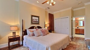 A bedroom with a large bed, a ceiling fan, a nightstand with a lamp, and a door leading to a bathroom. - 1bd, 1.5ba Historic District and River Front-Walk to Everything! (Savannah)