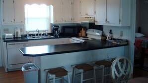 A kitchen with white cabinets, a microwave, a coffee maker, and a sink. There are bar stools and a trash can. - Shell House  - Less than a block to beach access and recently updated! (Sunset Beach)