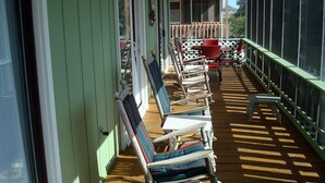 A covered porch with wooden chairs and a table, a ceiling fan, and a view of a house in the background. - Shell House  - Less than a block to beach access and recently updated! (Sunset Beach)