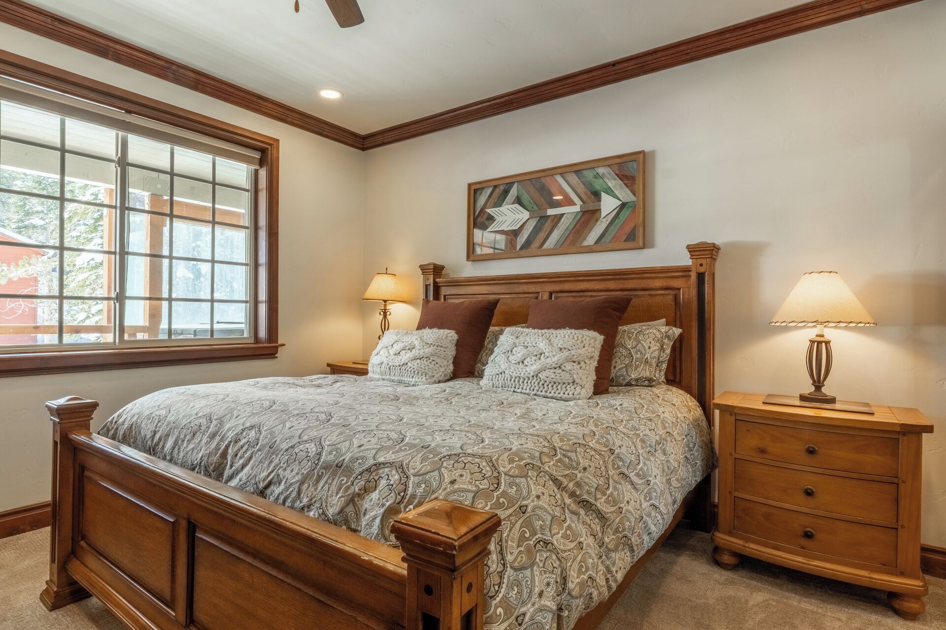 A bedroom with a wooden bed, two bedside tables with lamps, a window with blinds, and a painting on the wall.