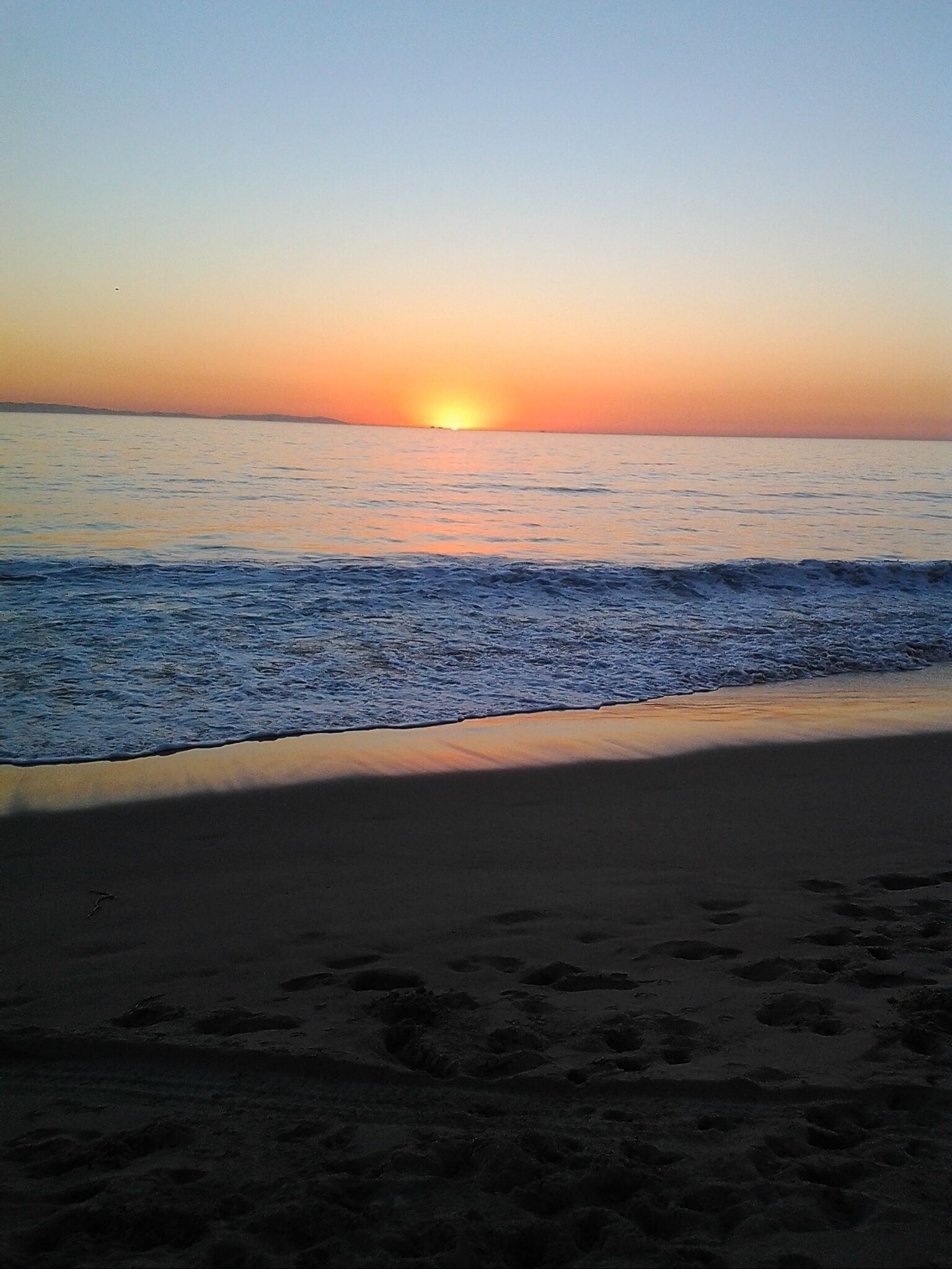 Una playa con el sol poniéndose sobre el océano, creando un ambiente tranquilo y sereno.