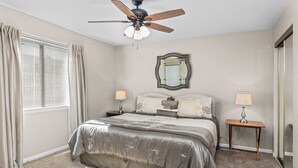 A bedroom with a bed, two bedside tables, a ceiling fan, a mirror, and a window with curtains. - Lazy Days V-01 - Five Bedroom Apartment, Sleeps 12 (Osage Beach)
