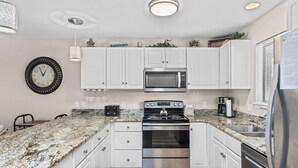 A kitchen with white cabinets, a granite countertop, stainless steel appliances, and a clock on the wall. - Lazy Days V-01 - Five Bedroom Apartment, Sleeps 12 (Osage Beach)