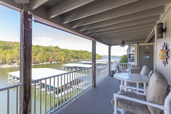 Un balcon abrité offrant une vue sur un lac et un quai, avec des meubles d’extérieur blancs et un élément décoratif mural.