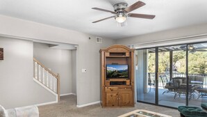 A living room with a wooden entertainment center, a glass coffee table, a sofa, and a balcony with outdoor furniture. - Lazy Days V-01 - Five Bedroom Apartment, Sleeps 12 (Osage Beach)