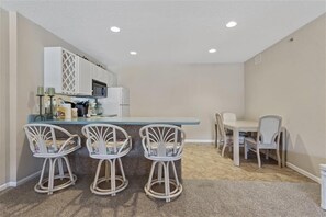 Compact kitchen area with microwave and white cabinetry, featuring a dining table and four chairs.