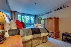 Une chambre Ă coucher avec un lit, une armoire en bois, un bureau et une fenĂȘtre donnant sur des arbres.