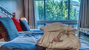 Un lit avec un peignoir blanc, des oreillers et une vue sur les arbres par la fenêtre.