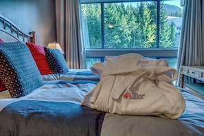 A bed with a white robe, pillows, and a view of trees through a window.