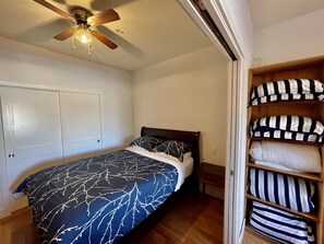 Un dormitorio con cama, ventilador de techo, armario y estante con almohadas.