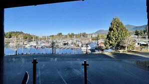 A marina with boats docked, a clear sky, and a view of a town and mountains in the distance.