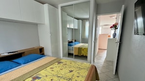 Un dormitorio con cama, armario, espejo y puerta que da a un baño.