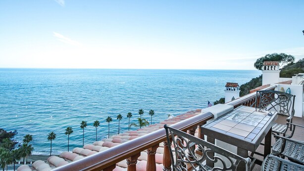 Ein Balkon mit Blick auf das Meer, Palmen und einem Tisch mit Fliesen.