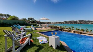 Un área junto a la piscina con sillones de descanso, una pequeña mesa con bebidas y vistas al mar.