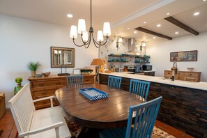 A modern kitchen with a wooden island, a dining area with a round table, and a chandelier.