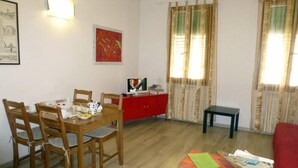 Un comedor con una mesa y sillas de madera, un armario rojo y un televisor sobre un mueble.