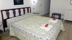 Un dormitorio con colcha estampada, cabecera de madera, mesita de noche, una pequeña mesa redonda y un aparador blanco.