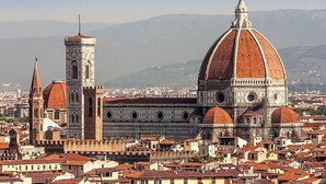 Una catedral histórica con una cúpula destacada y un campanario, rodeada de edificios urbanos densamente agrupados.